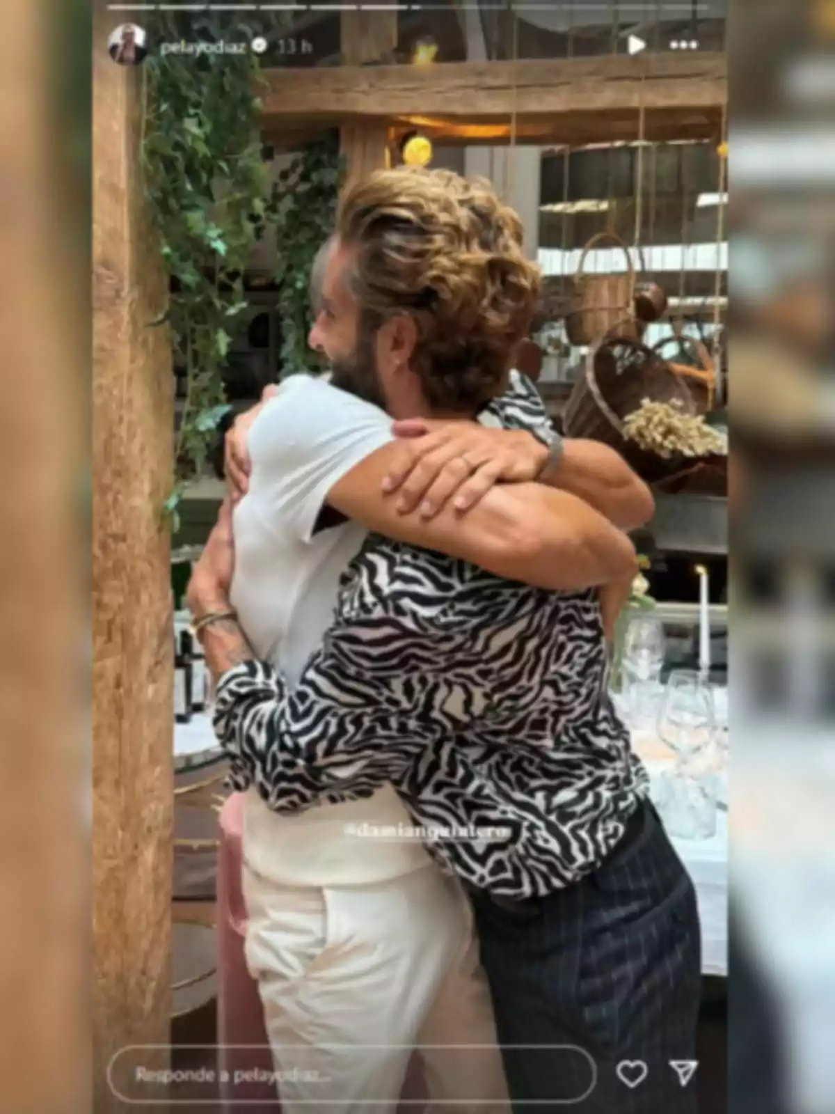 Pelayo Díaz i Damián Quintero abraçant-se en un ambient interior decorat amb plantes i taules parades Pelayo Díaz i Damián Quintero abraçant-se en un ambient interior decorat amb plantes i taules parades