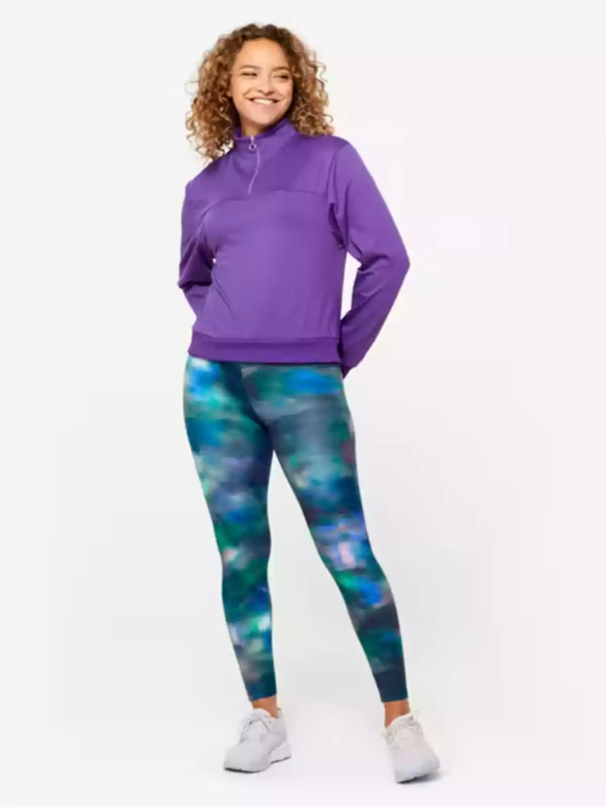 Dona somrient amb dessuadora morada i leggings amb estampat colorit, de peu sobre un fons clar.