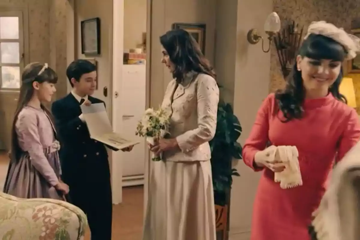 Quatre persones elegantment vestides interactuen en una sala decorada de manera clàssica, una dona sosté un ram de flors mentre un nen li mostra un llibre obert i una nena observa somrient, al fons una altra dona amb vestit rosa somriu mentre sosté uns guants. Captura de 'Sueños de libertad' Quatre persones elegantment vestides interactuen en una sala decorada de manera clàssica, una dona sosté un ram de flors mentre un nen li mostra un llibre obert i una nena observa somrient, al fons una altra dona amb vestit rosa somriu mentre sosté uns guants. Captura de 'Sueños de libertad'