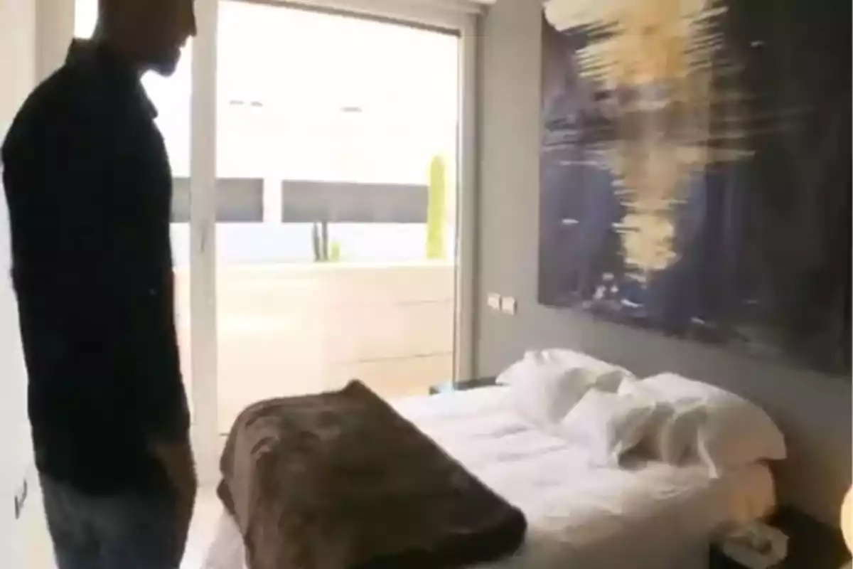 Gonzalo Miró dret en una habitació moderna amb un llit cobert per una manta marró i un gran quadre abstracte a la paret. Captura de 'Supercasas'. Gonzalo Miró dret en una habitació moderna amb un llit cobert per una manta marró i un gran quadre abstracte a la paret. Captura de 'Supercasas'.