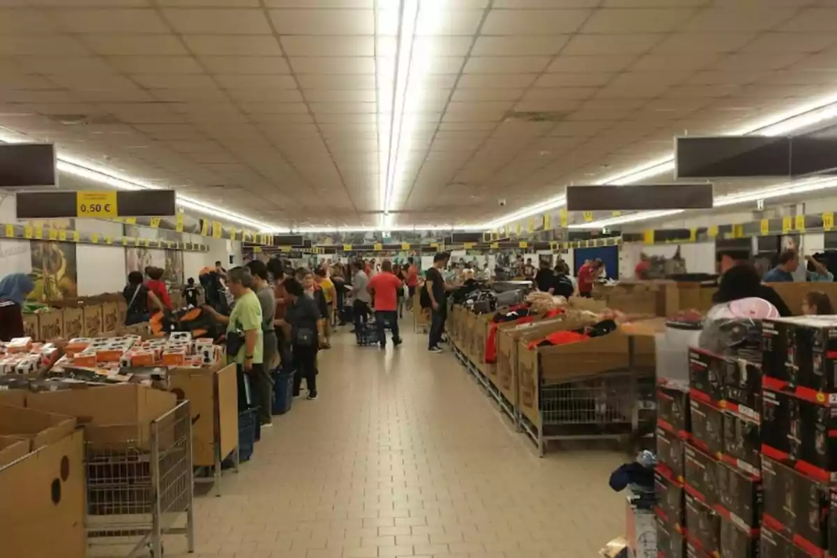 Persones comprant en un supermercat amb passadissos plens de productes i caixes de cartró. Persones comprant en un supermercat amb passadissos plens de productes i caixes de cartró.