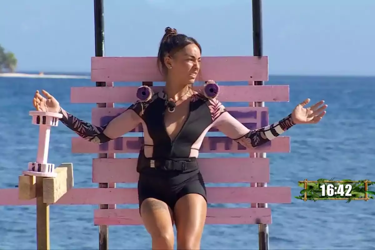 Anita amb vestit esportiu està asseguda en una estructura de fusta rosa davant del mar, amb els braços estesos i un cronòmetre a la cantonada inferior dreta. Captura de 'Supervivientes' Anita amb vestit esportiu està asseguda en una estructura de fusta rosa davant del mar, amb els braços estesos i un cronòmetre a la cantonada inferior dreta. Captura de 'Supervivientes'