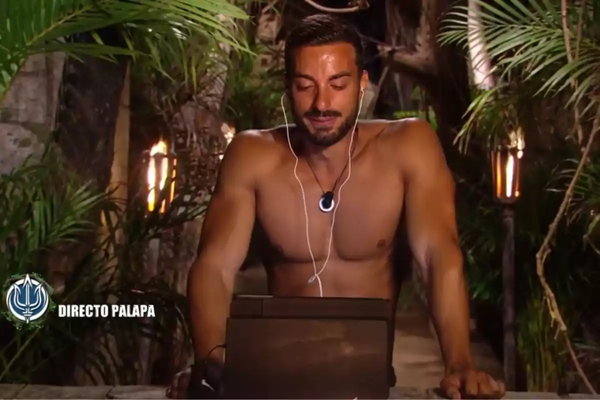 Borja González sense camisa està usant auriculars i mirant una pantalla en un entorn selvàtic il·luminat per torxes. Captura de 'Supervivientes'. Borja González sense camisa està usant auriculars i mirant una pantalla en un entorn selvàtic il·luminat per torxes. Captura de 'Supervivientes'.