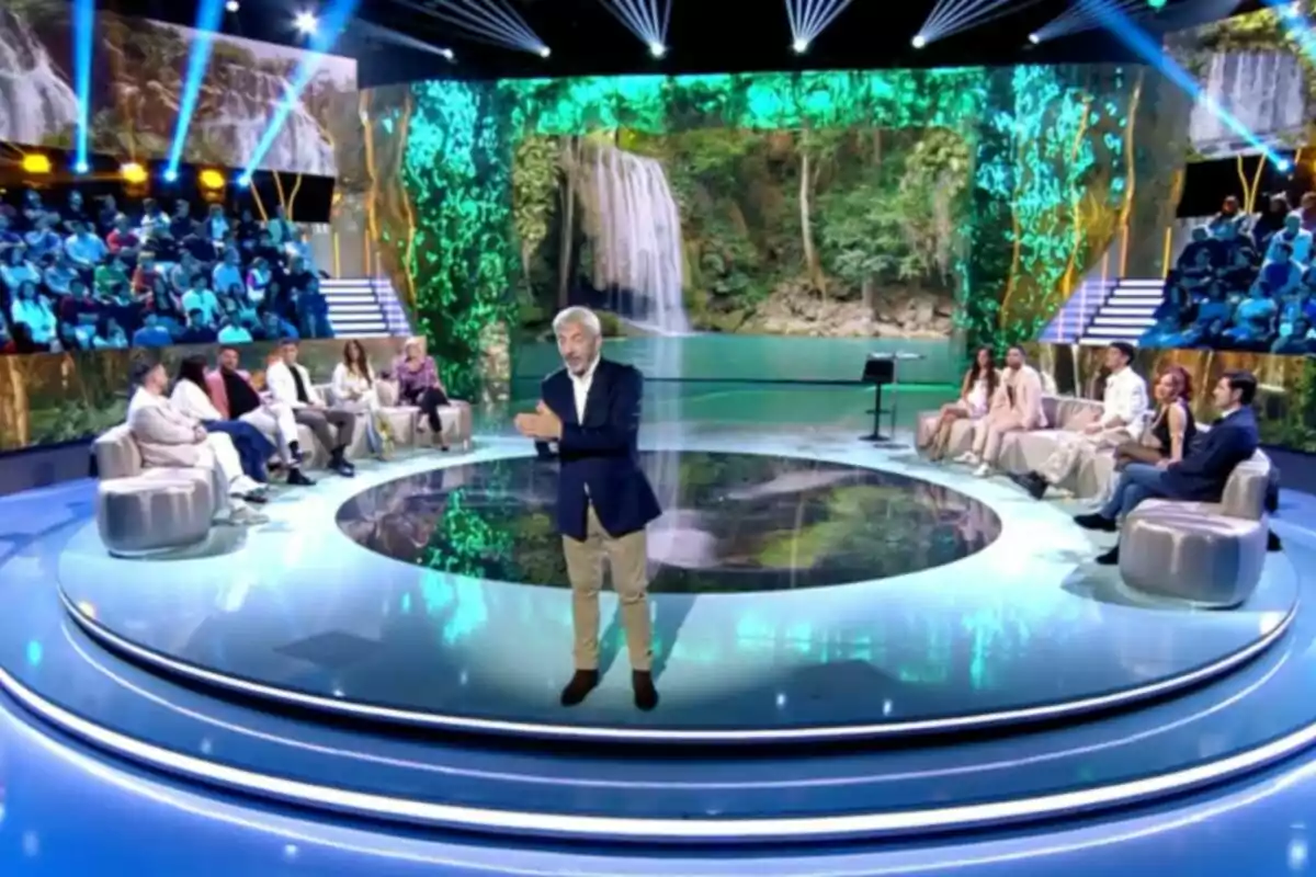 Carlos Sobera és en un estudi de televisió amb un fons de cascada i públic assegut al voltant. Captura de 'Supervivientes'. Carlos Sobera és en un estudi de televisió amb un fons de cascada i públic assegut al voltant. Captura de 'Supervivientes'.