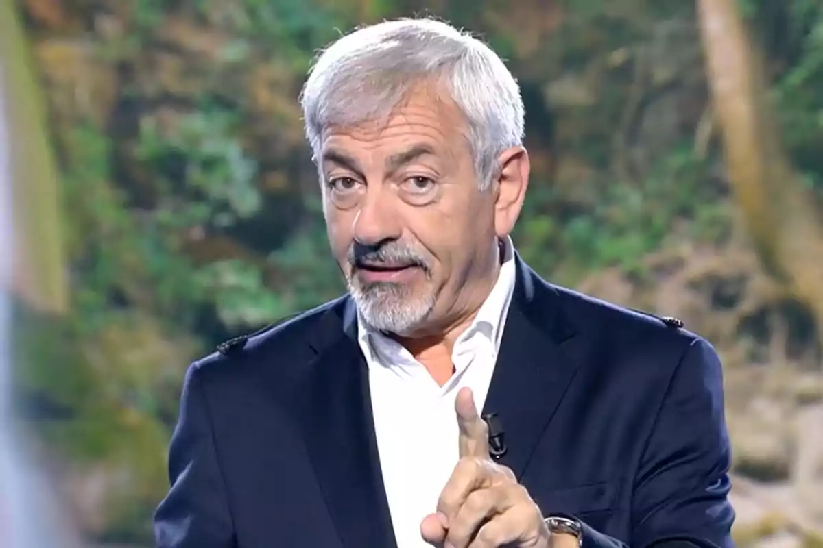 Carlos Sobera està parlant i gesticulant amb el dit índex aixecat, vestint un vestit fosc i camisa blanca, amb un fons de natura desenfocat. Captura de 'Supervivientes'. Carlos Sobera està parlant i gesticulant amb el dit índex aixecat, vestint un vestit fosc i camisa blanca, amb un fons de natura desenfocat. Captura de 'Supervivientes'.
