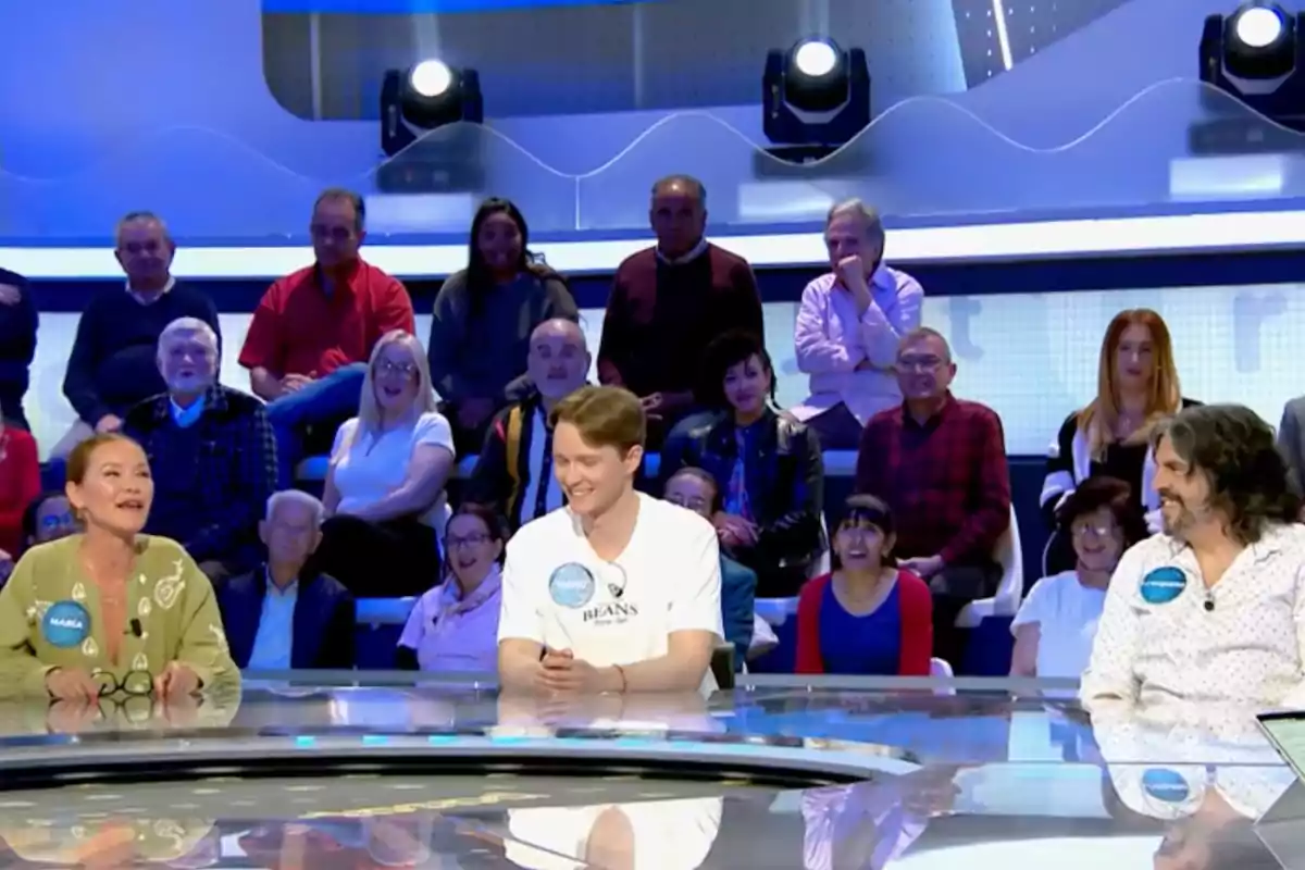 María Esteve, Manu i J. J. Vaquero asseguts en una taula rodona en un programa de televisió amb públic somrient al fons. Captura de 'Pasapalabra'
