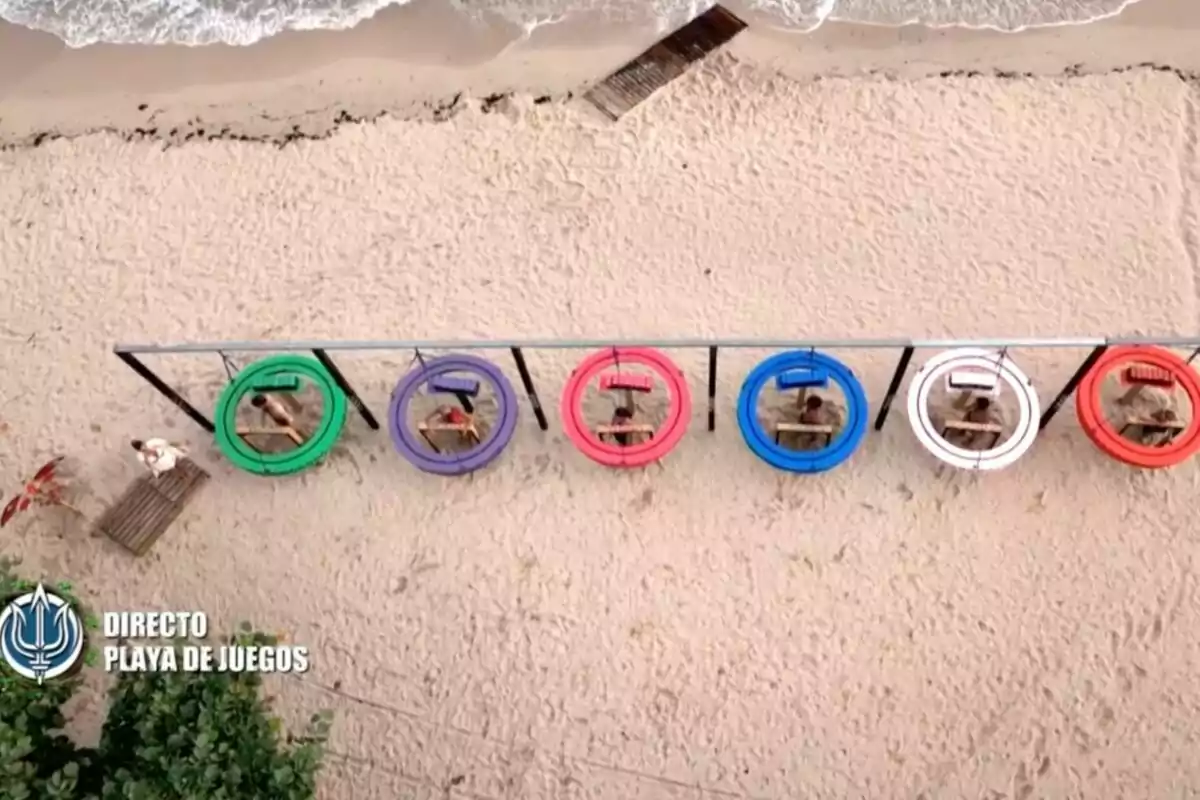 Vista aèria d’una platja amb sis persones assegudes dins de cèrcols de colors suspesos sobre la sorra davant del mar. Captura de ‘Supervivientes’. Vista aèria d’una platja amb sis persones assegudes dins de cèrcols de colors suspesos sobre la sorra davant del mar. Captura de ‘Supervivientes’.