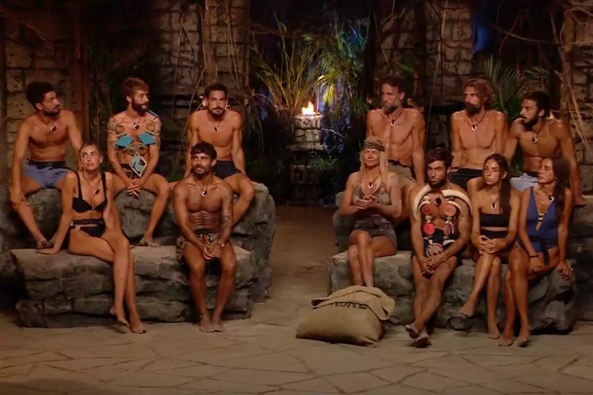 Un grup de persones assegudes en un entorn d'estil tribal amb una torxa encesa al fons. Captura de 'Supervivientes'. Un grup de persones assegudes en un entorn d'estil tribal amb una torxa encesa al fons. Captura de 'Supervivientes'.