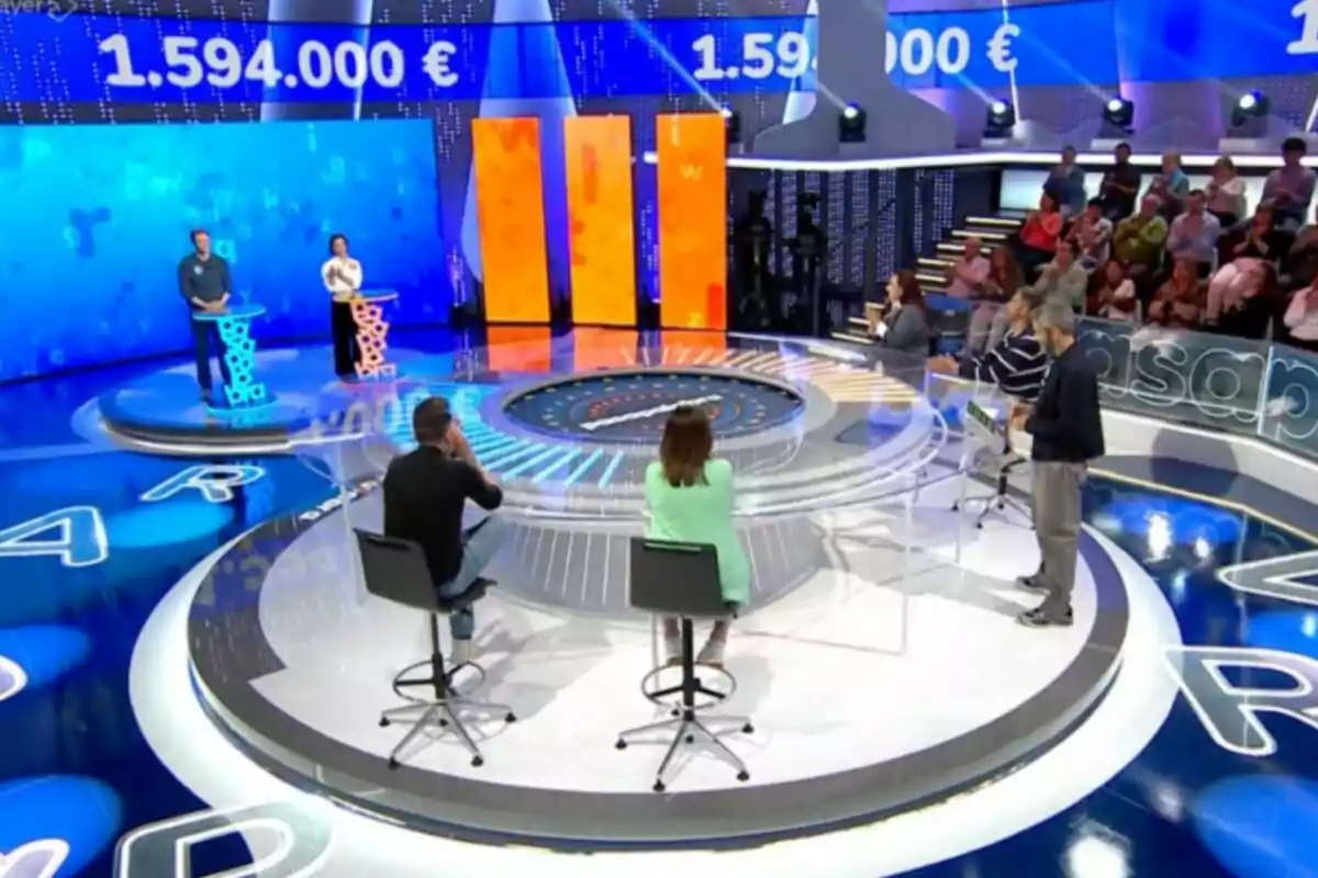 Un programa de concurs en un estudi de televisió amb participants drets darrere de faristols il·luminats i un públic observant des de les grades. Captura de 'Pasapalabra'. Un programa de concurs en un estudi de televisió amb participants drets darrere de faristols il·luminats i un públic observant des de les grades. Captura de 'Pasapalabra'.