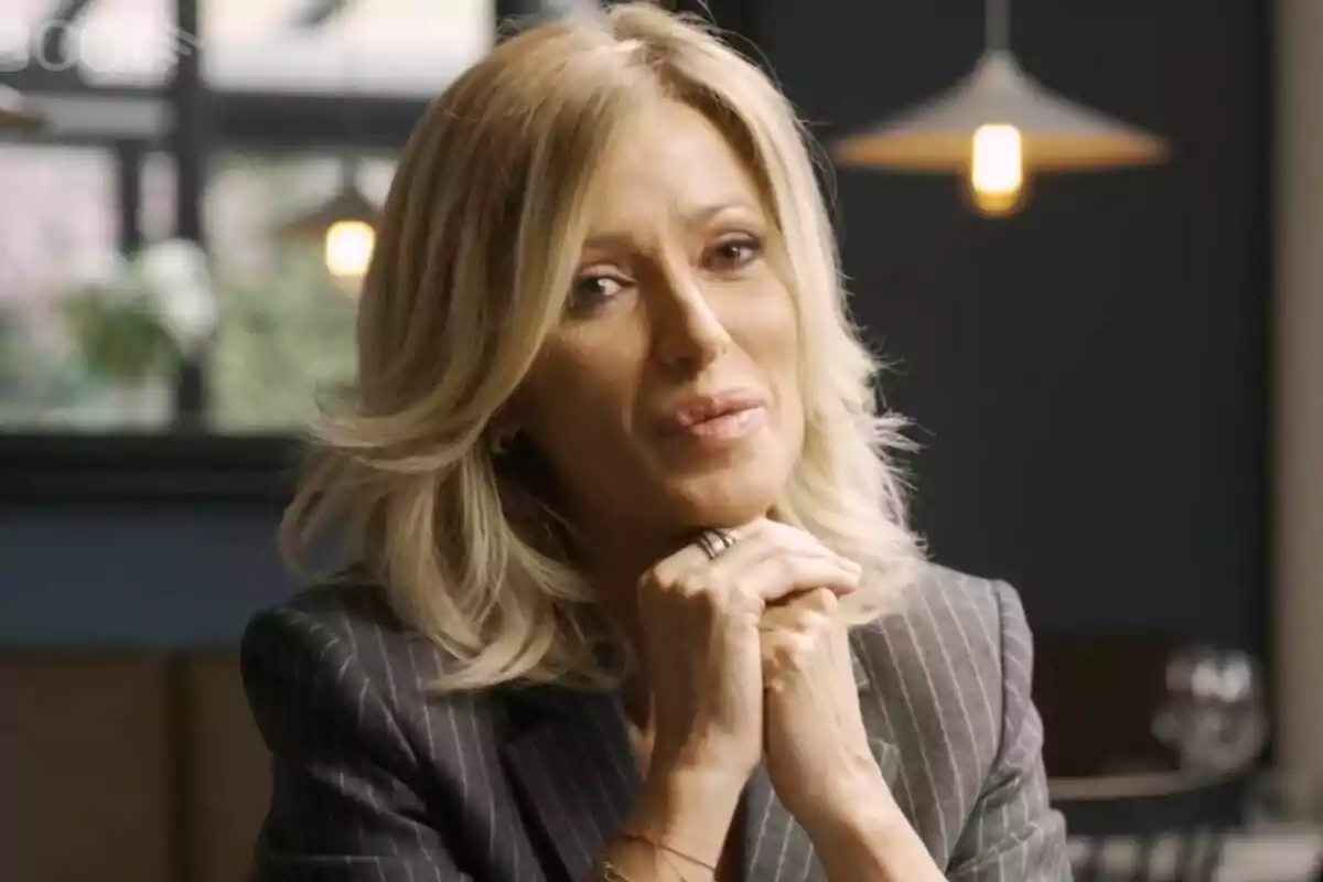 Susanna Grisoo amb cabell ros i expressió serena, vestida amb un vestit de ratlles, en un ambient interior amb llums penjants a Col·lapse. Susanna Grisoo amb cabell ros i expressió serena, vestida amb un vestit de ratlles, en un ambient interior amb llums penjants a Col·lapse.