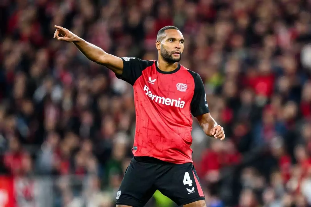 Un jugador de fútbol con uniforme rojo y negro señala hacia un lado en un estadio lleno de espectadores.