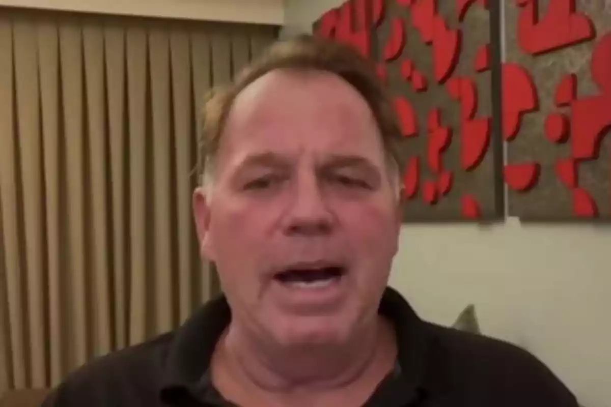 Thomas Markle Jr. in a dark jersey is speaking in front of a beige curtain and a wall decorated with red geometric shapes. Thomas Markle Jr. in a dark jersey is speaking in front of a beige curtain and a wall decorated with red geometric shapes.