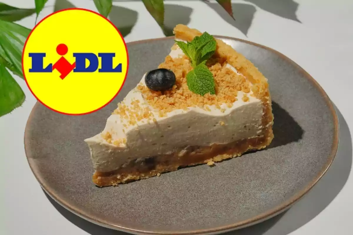 Una porció de pastís amb una base cruixent i una capa cremosa, decorada amb una fulla de menta i una baia, es presenta en un plat gris al costat d'un logotip de supermercat. Una porció de pastís amb una base cruixent i una capa cremosa, decorada amb una fulla de menta i una baia, es presenta en un plat gris al costat d'un logotip de supermercat.