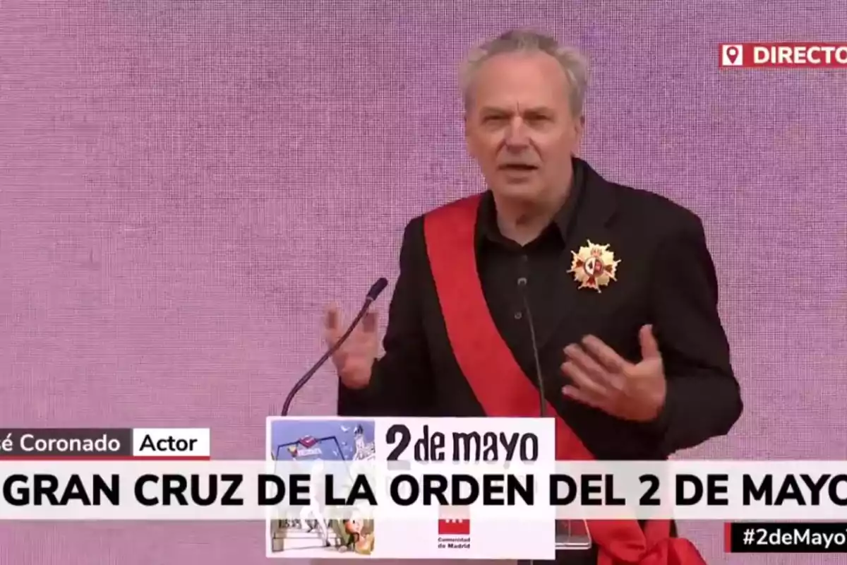 José Coronado amb una banda vermella i una medalla al pit parla en un faristol durant un esdeveniment del 2 de maig. José Coronado amb una banda vermella i una medalla al pit parla en un faristol durant un esdeveniment del 2 de maig.