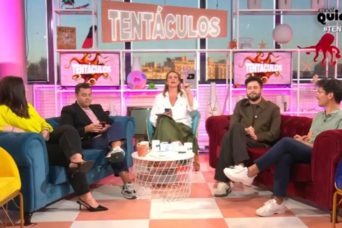 Un grup de persones està assegut en un plató de televisió acolorit amb el rètol Un grup de persones està assegut en un plató de televisió acolorit amb el rètol