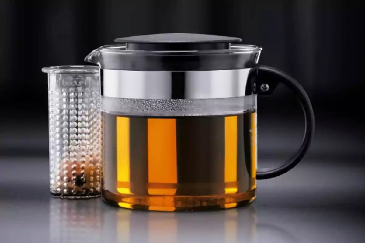 Tetera de vidre amb infusor de metall i mànec negre sobre una superfície grisa Tetera de vidre amb infusor de metall i mànec negre sobre una superfície grisa