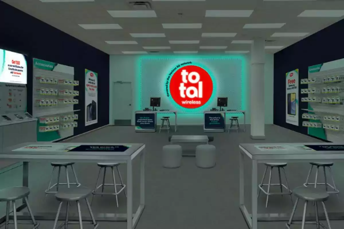 Una tienda de Total Wireless con mesas, taburetes y productos en exhibición, destacando un gran logotipo circular en la pared trasera. Una tienda de Total Wireless con mesas, taburetes y productos en exhibición, destacando un gran logotipo circular en la pared trasera.