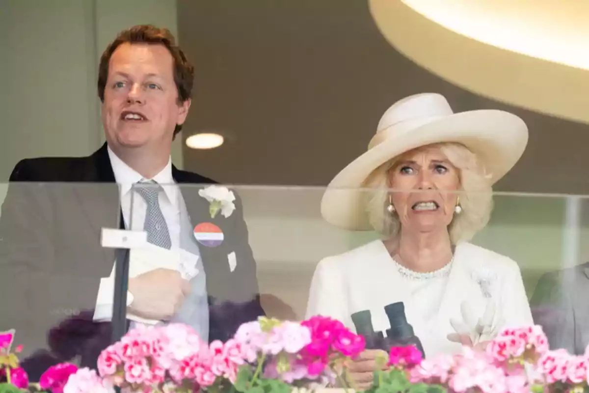 Elegantly dressed Tom Parker and Camila Parker watch something from a balcony decorated with pink flowers. Elegantly dressed Tom Parker and Camila Parker watch something from a balcony decorated with pink flowers.