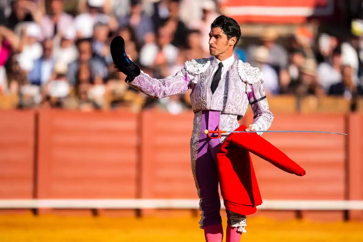 Un torero a la plaça sostenint la seva montera i capot mentre el públic observa. Un torero a la plaça sostenint la seva montera i capot mentre el públic observa.