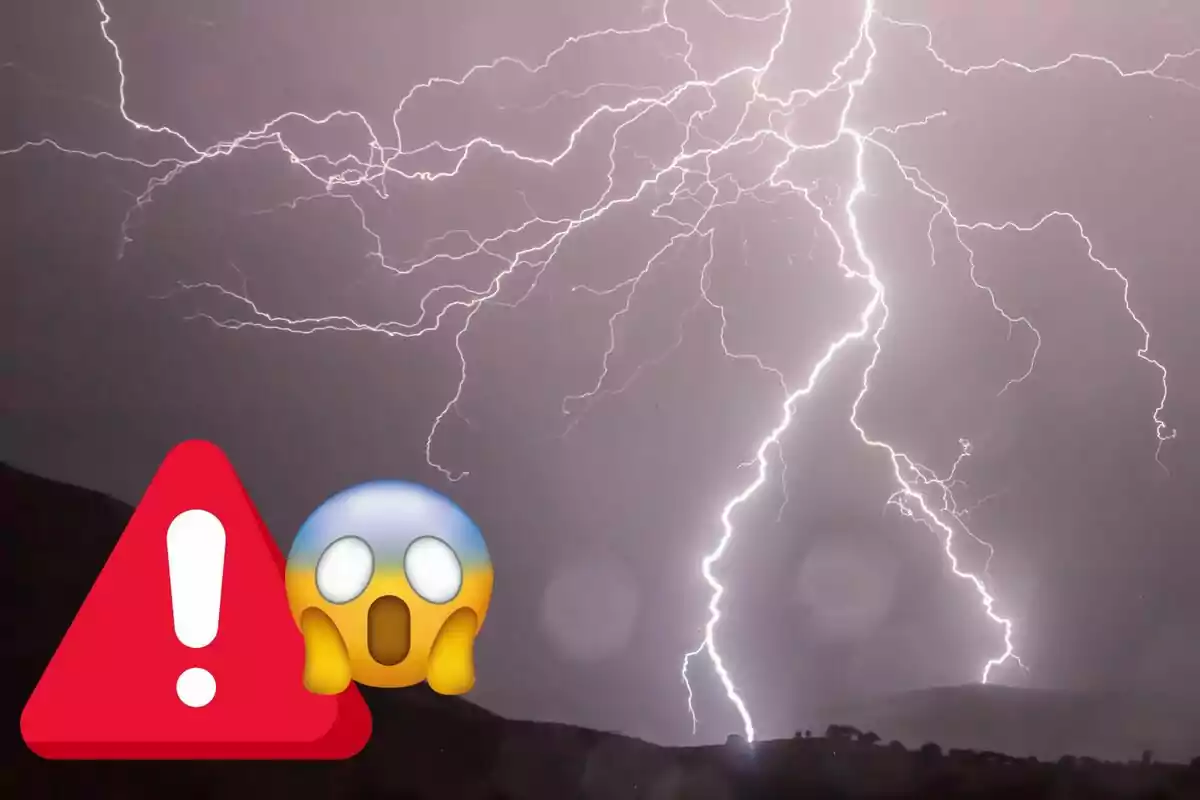 Cel nocturn il·luminat per diversos llamps amb un triangle d’advertència i un emoji d’espant en primer pla Cel nocturn il·luminat per diversos llamps amb un triangle d’advertència i un emoji d’espant en primer pla