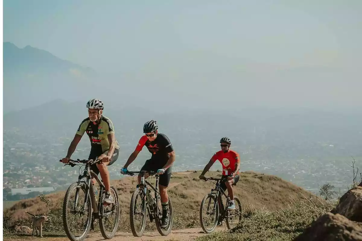 Tres persones amb un conjunt de ciclista i casc muntant amb bici per la muntanya