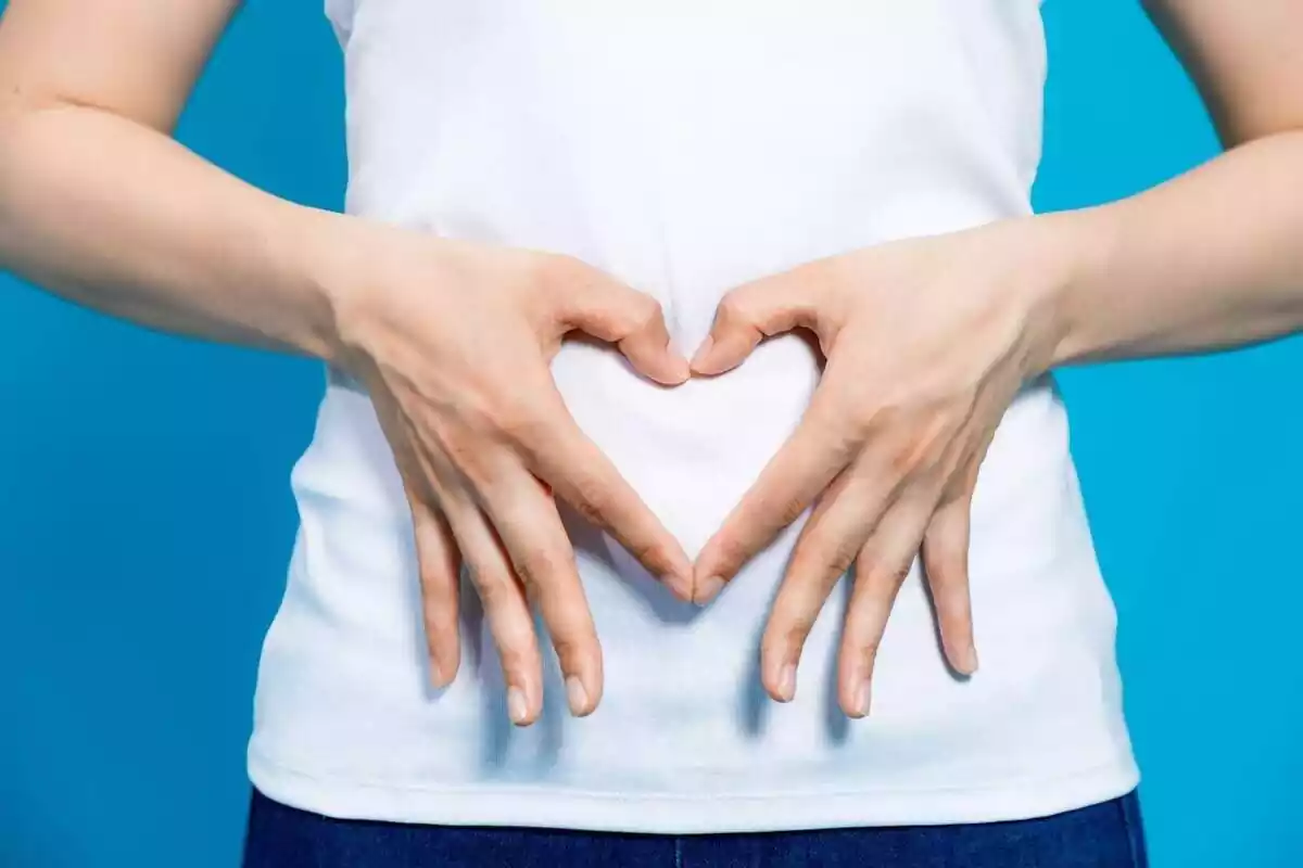 A woman making a heart to the stomach area with her fingers