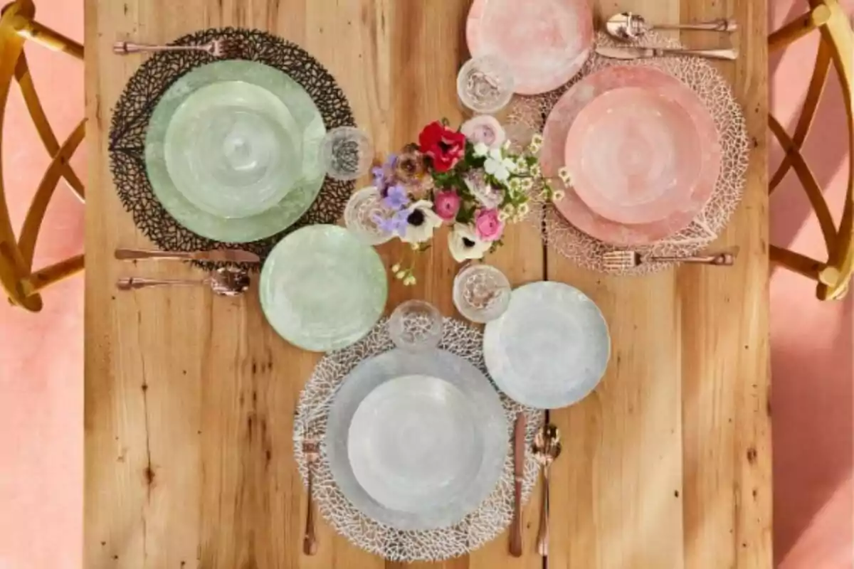 Mesa de madera con vajilla de colores pastel y un arreglo floral en el centro.