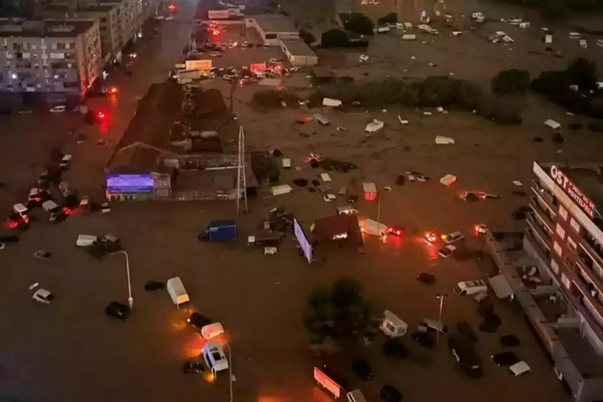 Vista aèria d?una ciutat inundada durant la nit amb vehicles submergits i llums d?emergència encesos.