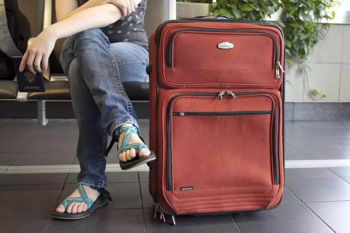 Una persona asseguda esperant amb una maleta al costat