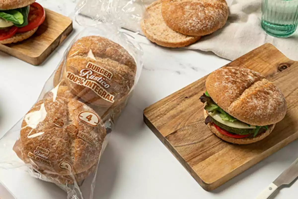 Un paquet de pa rústic integral al costat d'una hamburguesa amb ingredients frescos sobre una taula de fusta. Un paquet de pa rústic integral al costat d'una hamburguesa amb ingredients frescos sobre una taula de fusta.
