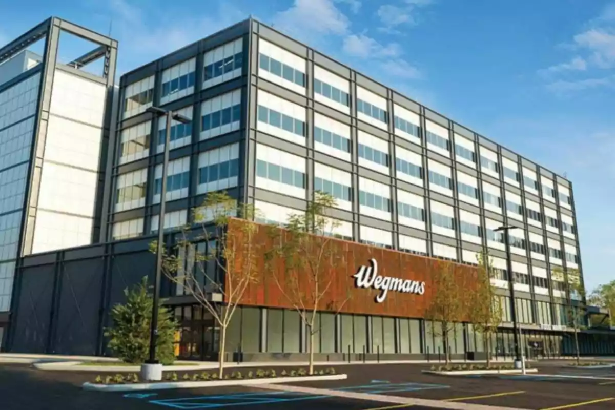 Edificio moderno de varios pisos con el letrero Wegmans en la fachada y un estacionamiento vacío al frente Edificio moderno de varios pisos con el letrero Wegmans en la fachada y un estacionamiento vacío al frente