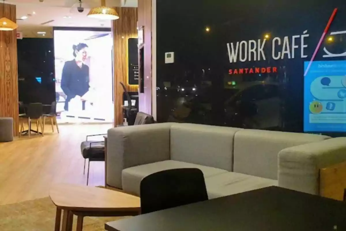 La imatge mostra l´interior d´un Work Café Santander, amb un sofà gris, una taula de fusta i cadires en un ambient modern i ben il·luminat. La imatge mostra l´interior d´un Work Café Santander, amb un sofà gris, una taula de fusta i cadires en un ambient modern i ben il·luminat.