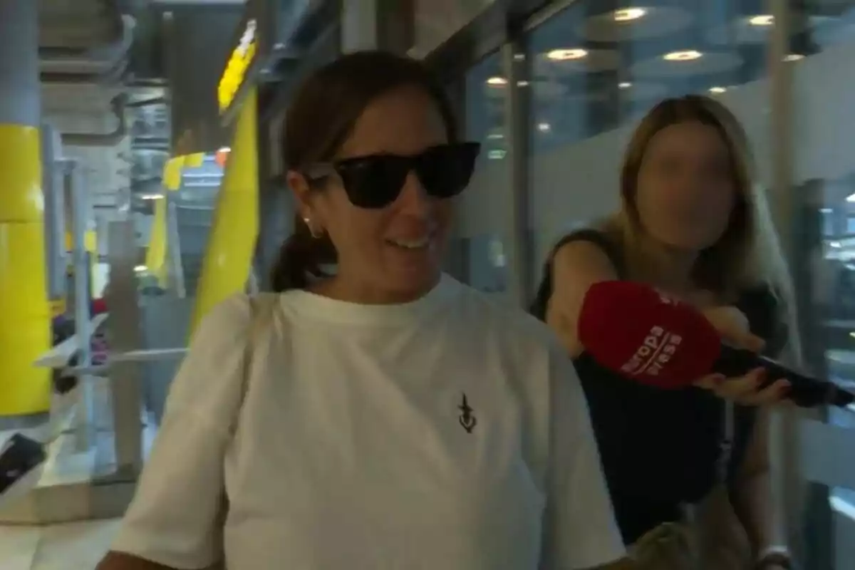 Anabel Pantoja con gafas de sol y camiseta blanca es entrevistada por una reportera que sostiene un micrófono rojo de Europa Press en un entorno urbano con elementos amarillos y grises. Captura de YouTube del 29 de julio de 2024