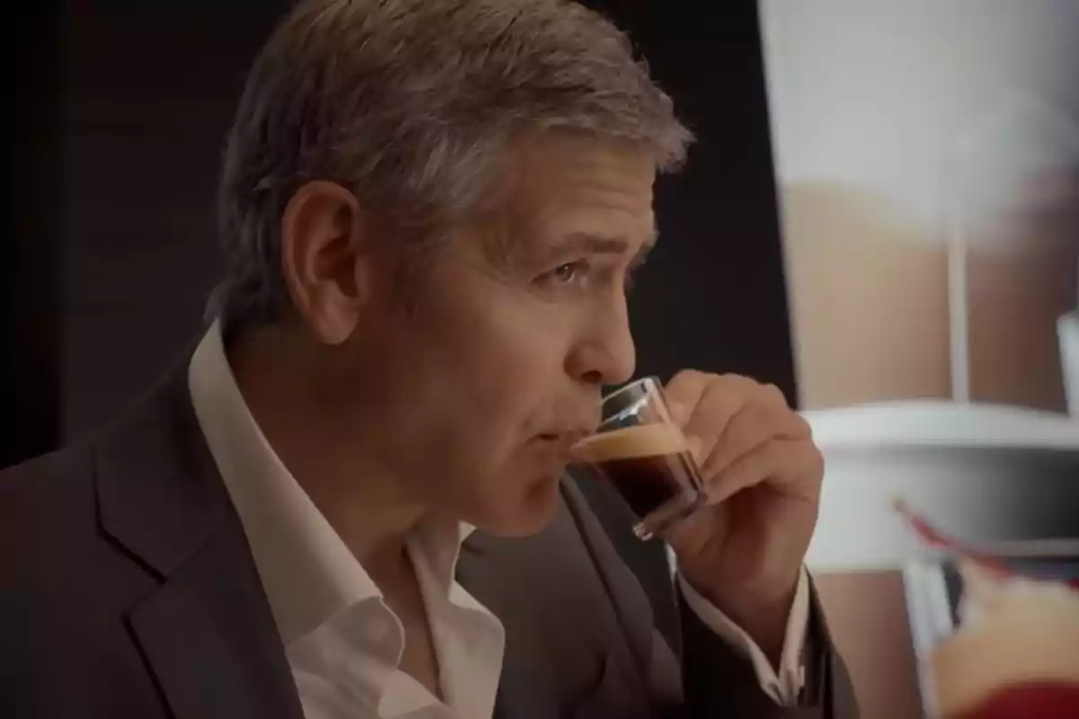 George Clooney dressed in a suit drinking an espresso coffee from a glass cup George Clooney dressed in a suit drinking an espresso coffee from a glass cup