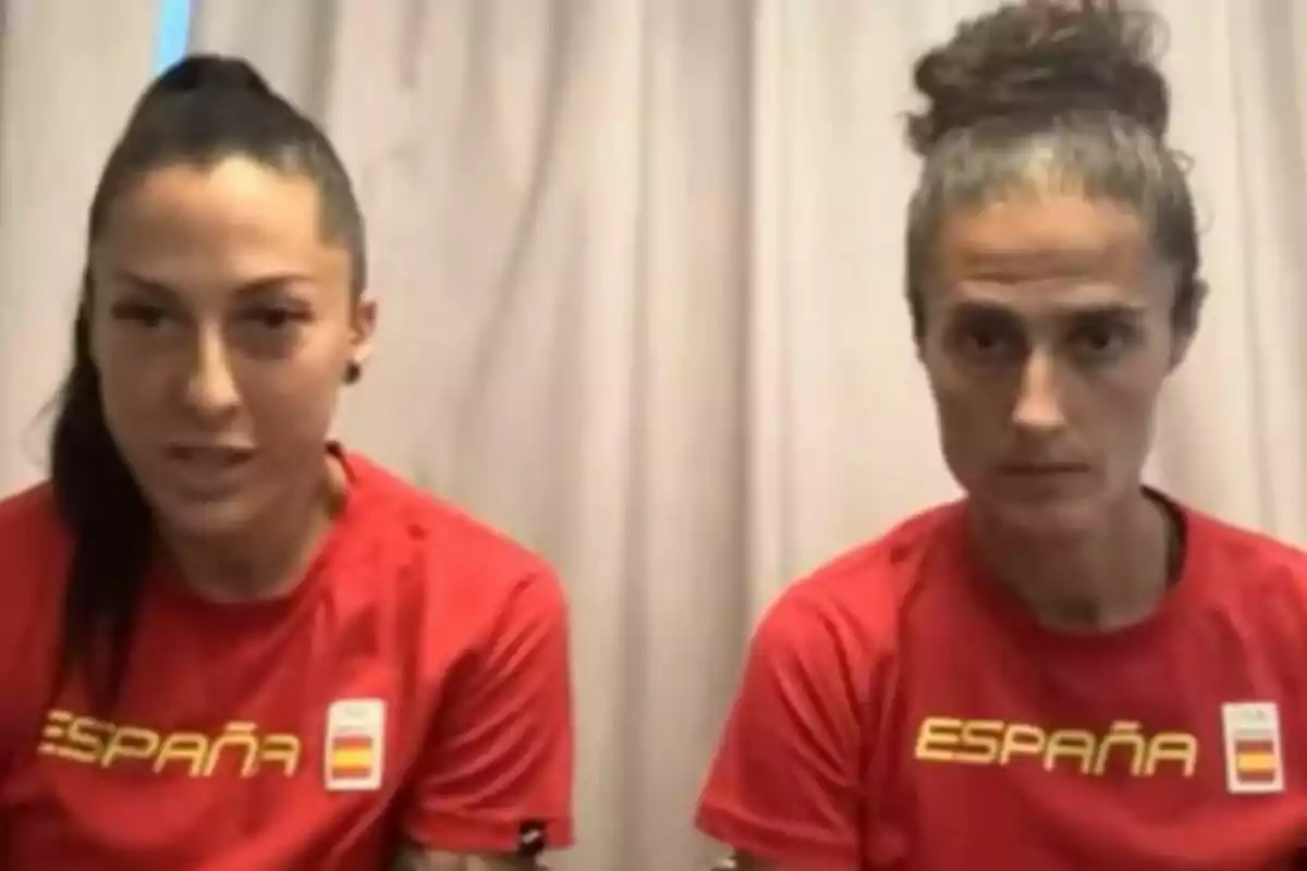 Jenni Hermoso y Montse Tomé con camisetas rojas de España están sentadas frente a una cortina beige. Jenni Hermoso y Montse Tomé con camisetas rojas de España están sentadas frente a una cortina beige.
