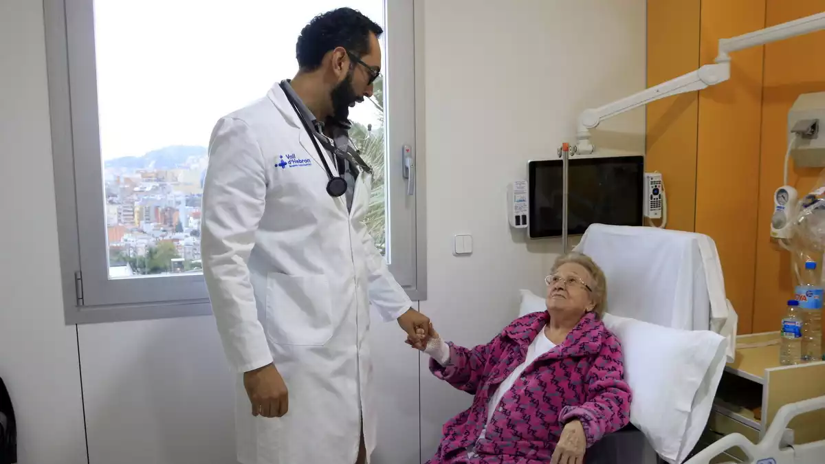 Eulalia, una pacient de 96 anys, s'agafa de la mà del doctor a l'habitació de la Unitat de Fragilitat conjunta de Vall d'Hebron i Sant Rafael