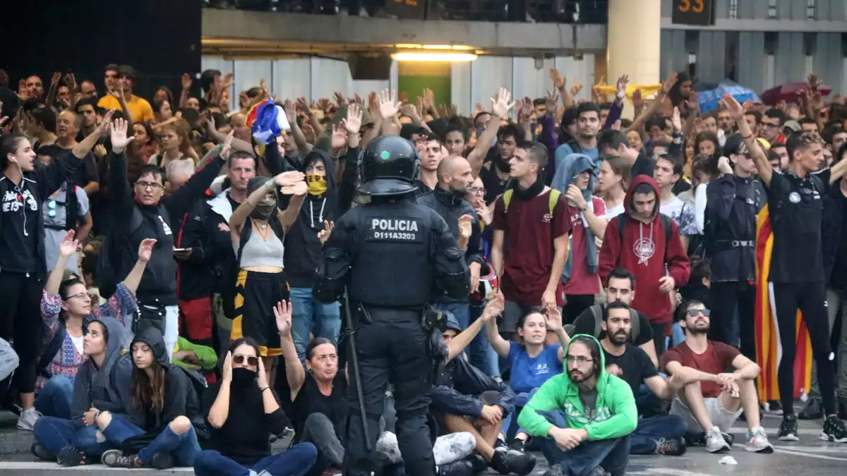 Un grup de manifestants a l'aeroport del Prat convocats per Tsunami Democràtic, darrere d'una línia policial, el 14 d'octubre del 2019