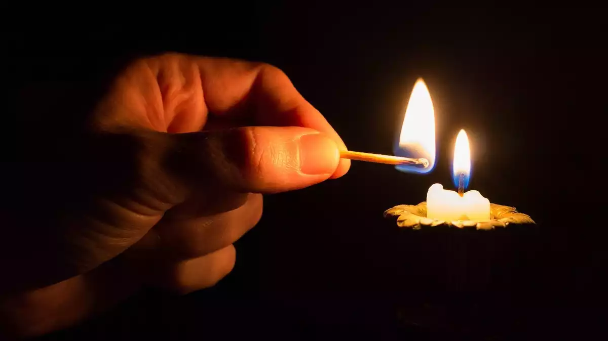 Una persona encenent una espelma amb un llumí perquè no hi ha llum