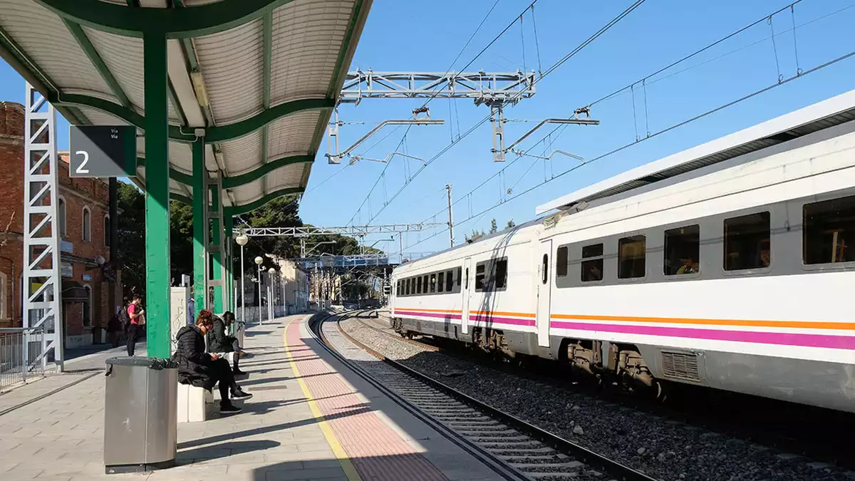 Un tren aturat a l'estació de Vila-seca mentre diversos viatgers s'esperen a l'andana.