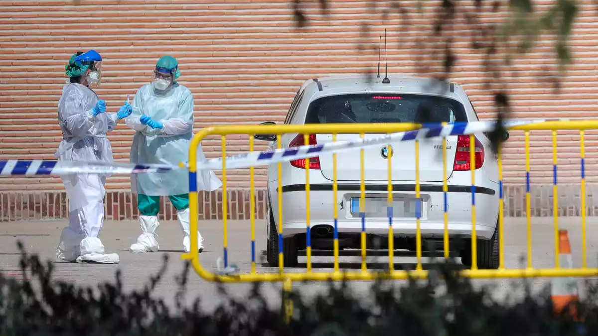 Imagen de dos profesionales de la salud conversando al lado de un coche con los trajes de protección