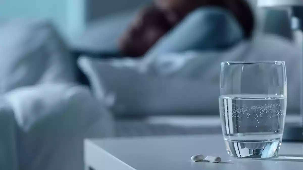 Un got amb una pastilla per dormir dins i una dona dormint