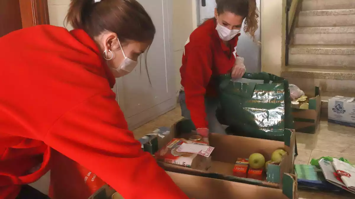 Dues tècniques de Creu Roja Tarragona posant el menjar en bosses de plàstic des del replà de casa del beneficiari, pero no entrar-hi com a mesura preventiva per la covid-19