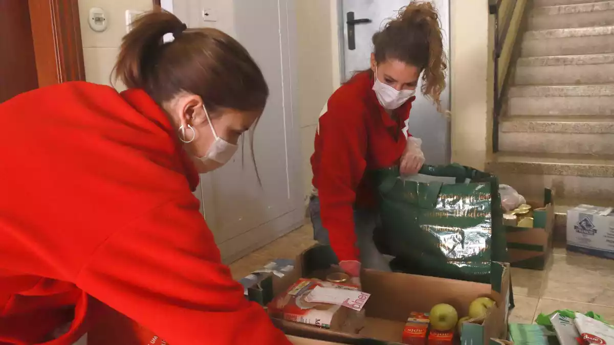 Dues tècniques de Creu Roja Tarragona posant el menjar en bosses de plàstic des del replà de casa del beneficiari, pero no entrar-hi com a mesura preventiva per la covid-19