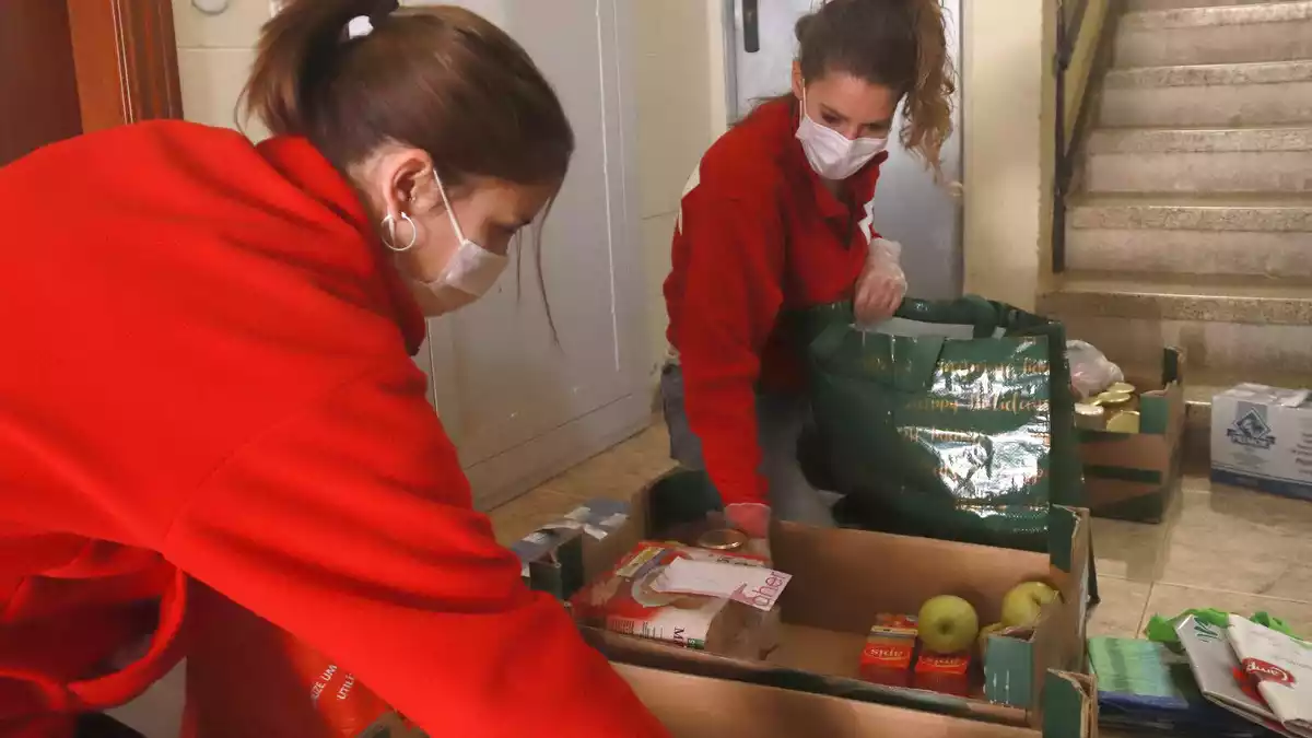 Pla mitjà de dues tècniques de Creu Roja Tarragona posant el menjar en bosses de plàstic des del replà de casa del beneficiari