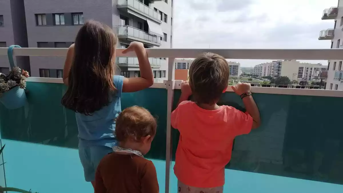 Imatge de tres nens mirant pel balcó a Lleida, el dia 18 d'abril de 2020.