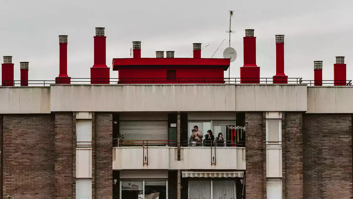 Imatge d'un bloc de pisos amb una família aplaudint des del balcó