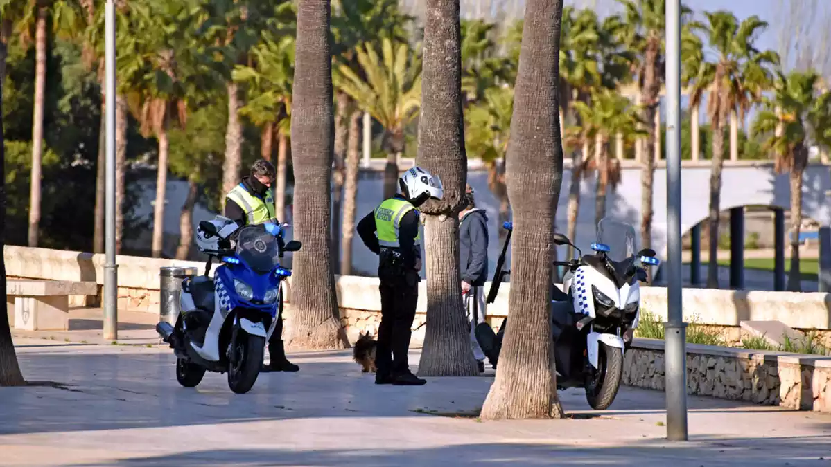Pla general de dos agents de la Policia Local fent una identificació al passeig marítim de Sant Carles de la Ràpita durant la Setmana Santa