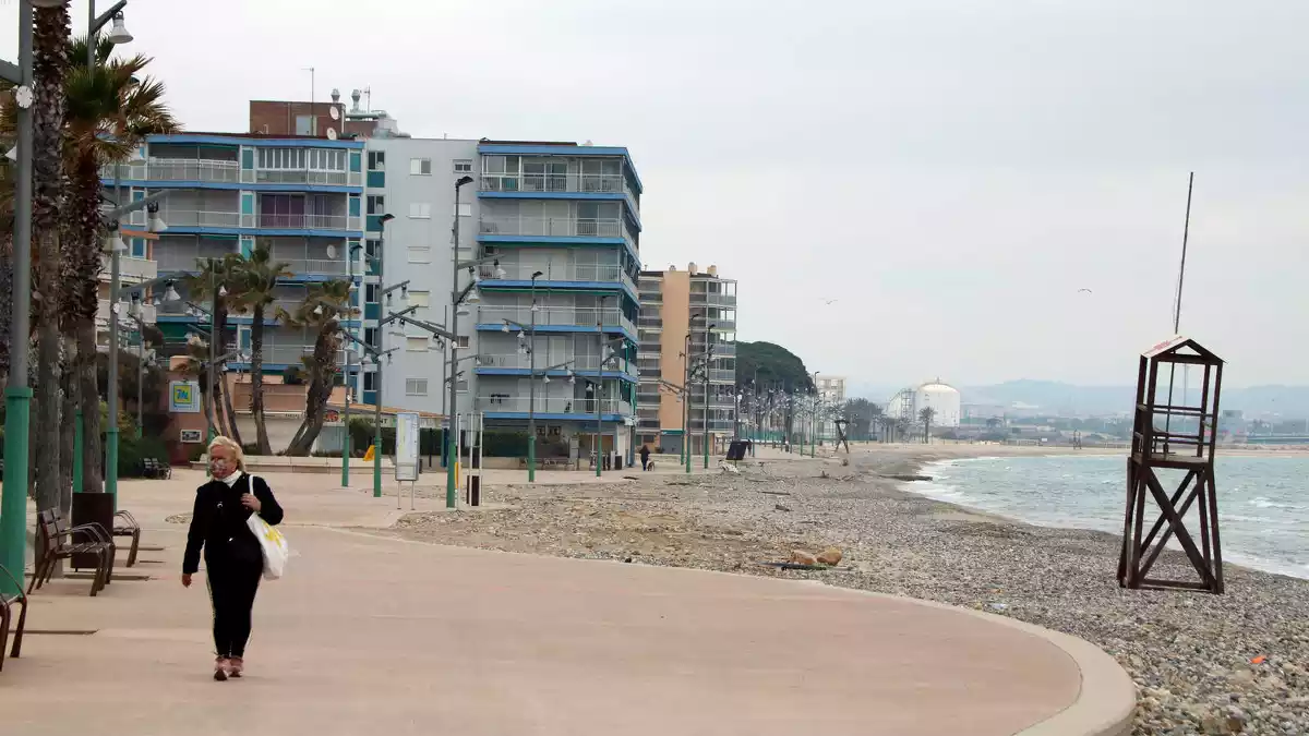 Pla general d'una dona caminant pel passeig marítim de la Pineda, amb la platja sense sorra