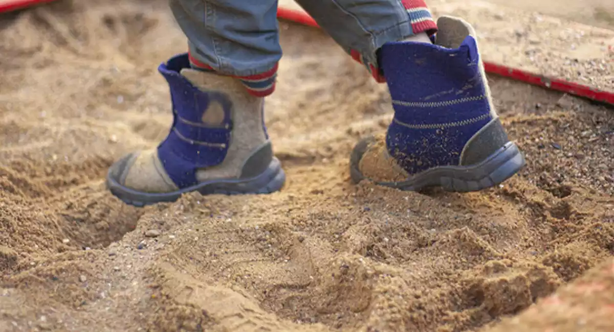 Imatge dels peus d'un nen que juga en un terreny de sorra en un parc