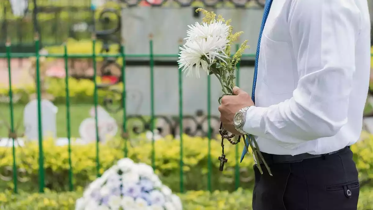 Hombre con flores ante una tumba